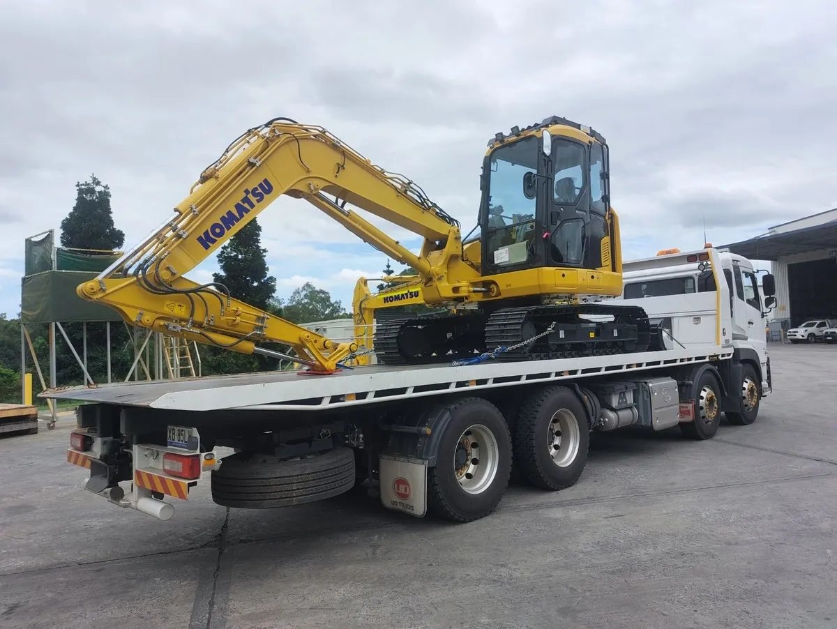 Truck transporting a yellow Komatsu excavator.